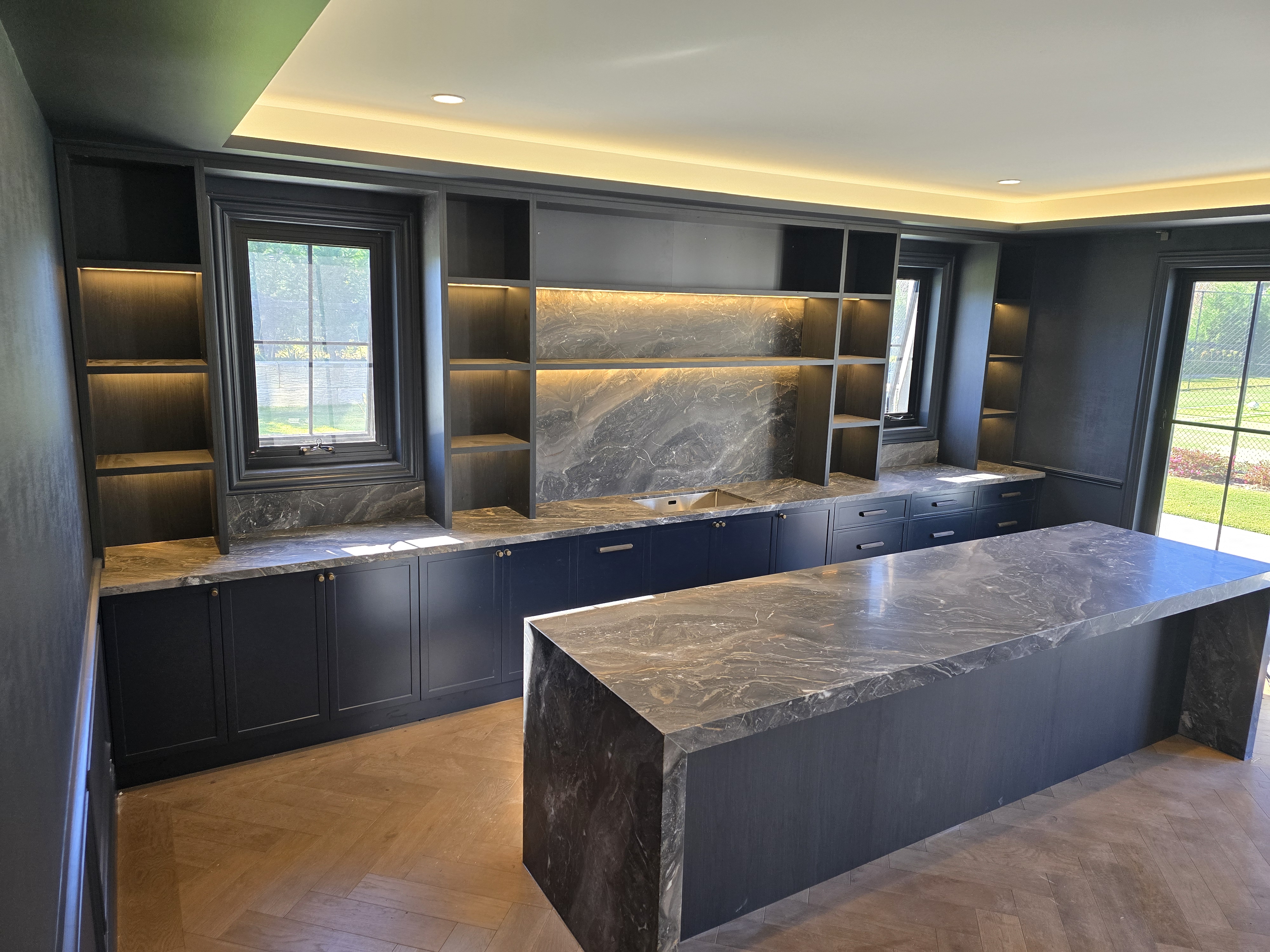Dark veined stone waterfall island with matching stone wall panels and illuminated shelves