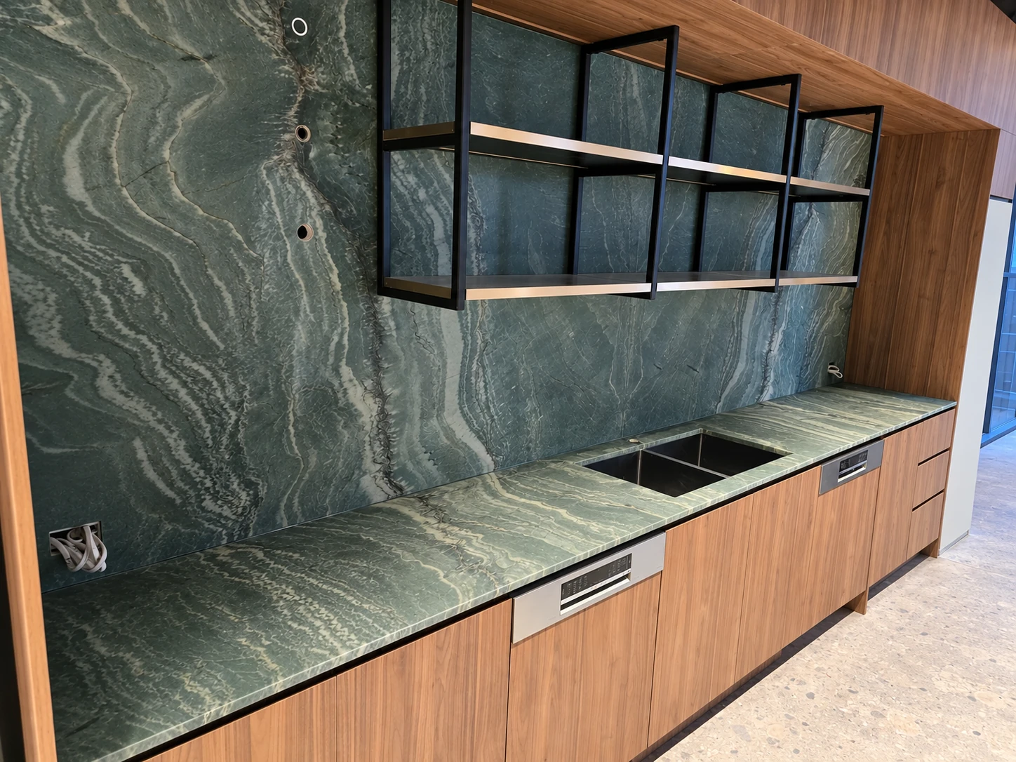 Green veined stone wall and benchtop with matching seams and timber cabinets